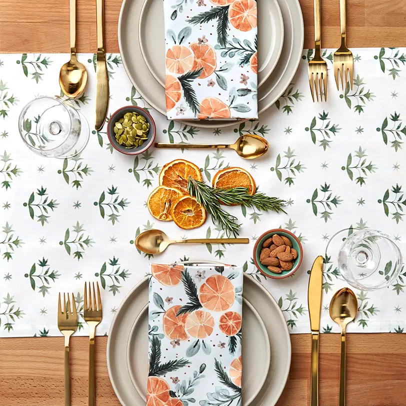 Table set with festive oranges and greenery runner and napkins.